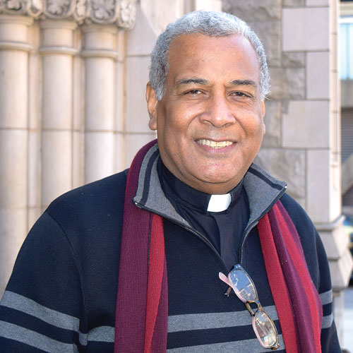 A headshot of Rev. Dr. Luis Barrios, smiling at the camera and wearing a red scarf