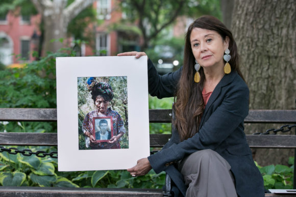 Marcia Esparza portrait, sitting on a bench holding up a color print of a photo from the Historical Memory Project archives